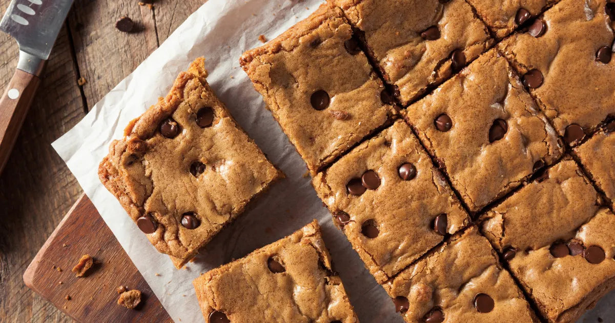 Freshly baked blondies cut into squares with chocolate chips, arranged on parchment paper for sharing